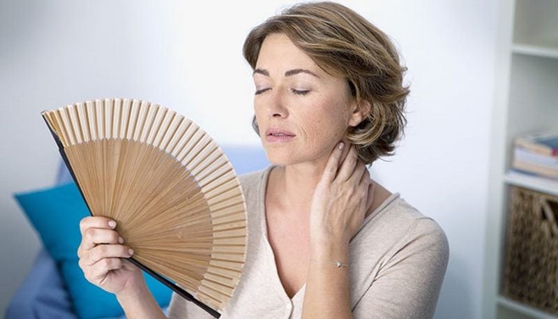 Image of a woman sweating and cooling with a fan due to high humidity