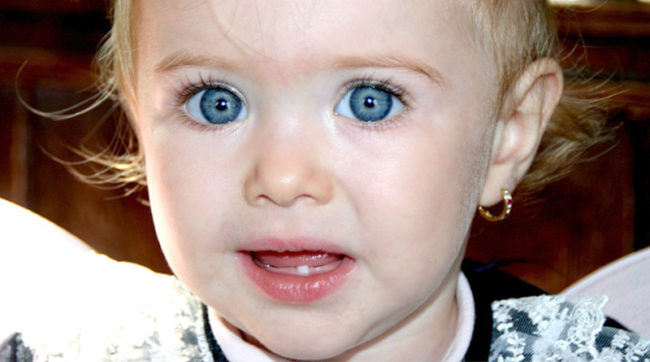 Маленькая девочка с голубыми глазами с одним молочным зубом