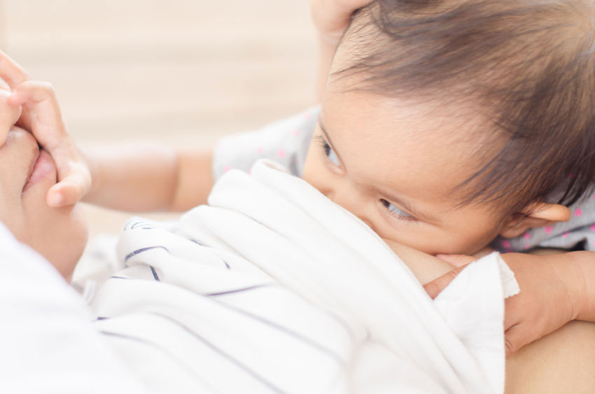 baby breastfeeding and reaching to touch her mother